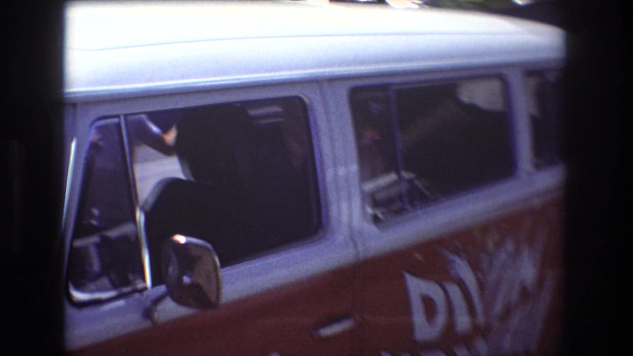 1977 Honolulu home-movie frame showing a red and white Diving Hawaii tour van with side windows and partial lettering, viewed through dark foreground framing.