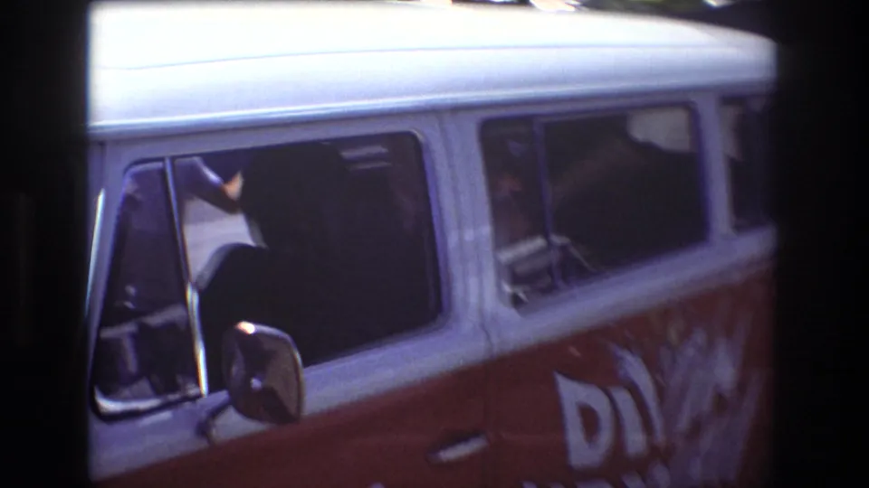 1977 Honolulu home-movie frame showing a red and white Diving Hawaii tour van with side windows and partial lettering, viewed through dark foreground framing.
