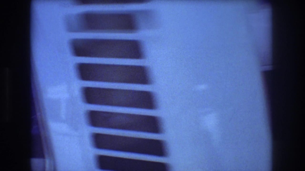 1977 Honolulu home-movie frame showing a pale truck cab detail with horizontal vents, blue low-light exposure, and dark film edges.