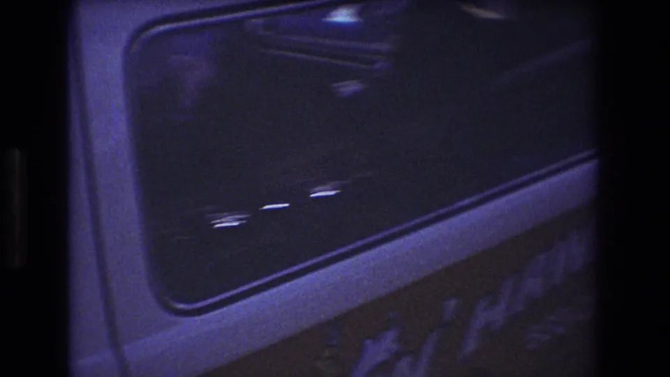 1977 Honolulu frame of a white truck cab side window at night, with a passenger faintly visible through dark glass and partial lettering below.