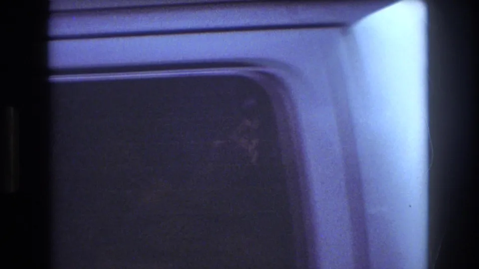 1977 Honolulu home-movie frame showing the truck cab corner and side window in blue night light, with a faint interior figure or reflection near the glass.