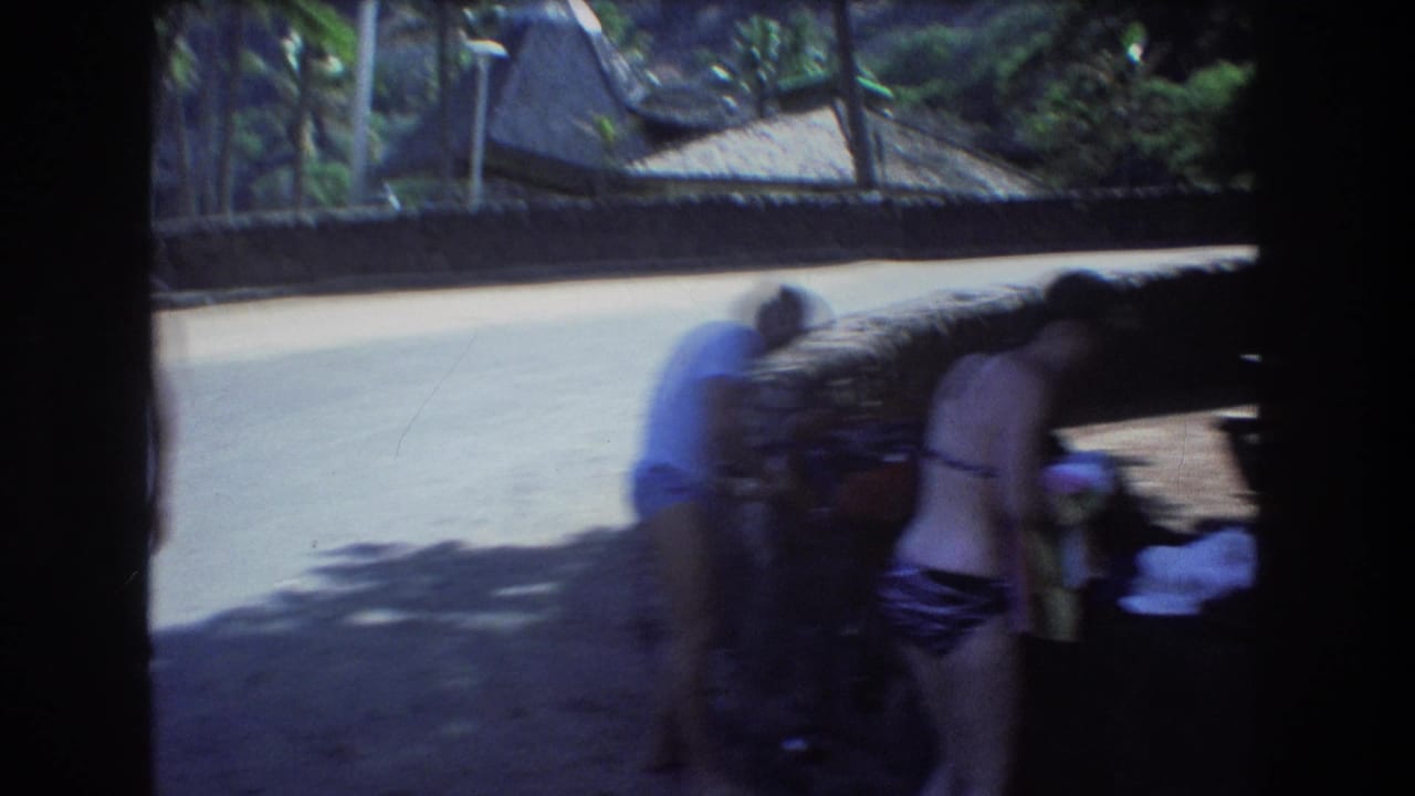 In 1977 Honolulu home-movie footage, adults stand near a stone picnic area as belongings are arranged beside a path and shaded foliage.