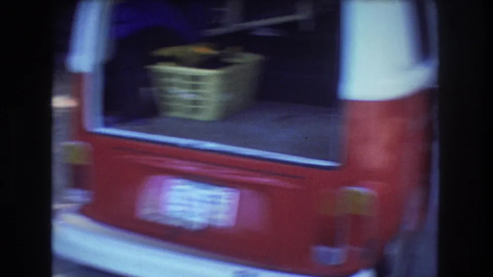 A red-and-white van with its rear door open appears in the 1977 Honolulu footage, with a yellow basket visible inside and picnic-area shade around it.