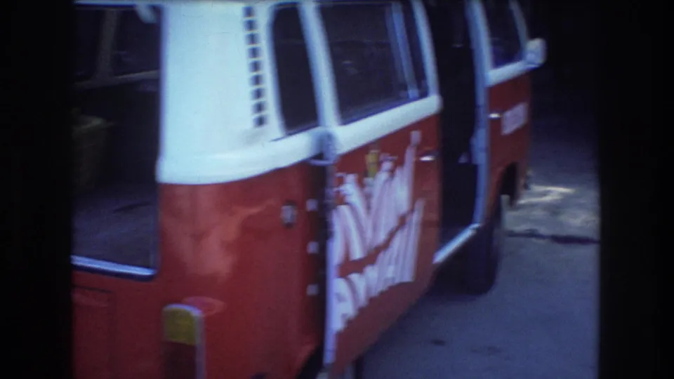 The side of a red-and-white van is seen parked near the Honolulu picnic area, with open doors, shaded pavement, and indistinct branded markings on the vehicle.