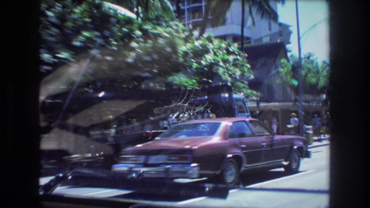View through a car windshield of a maroon sedan, tow truck, trees, and city buildings.