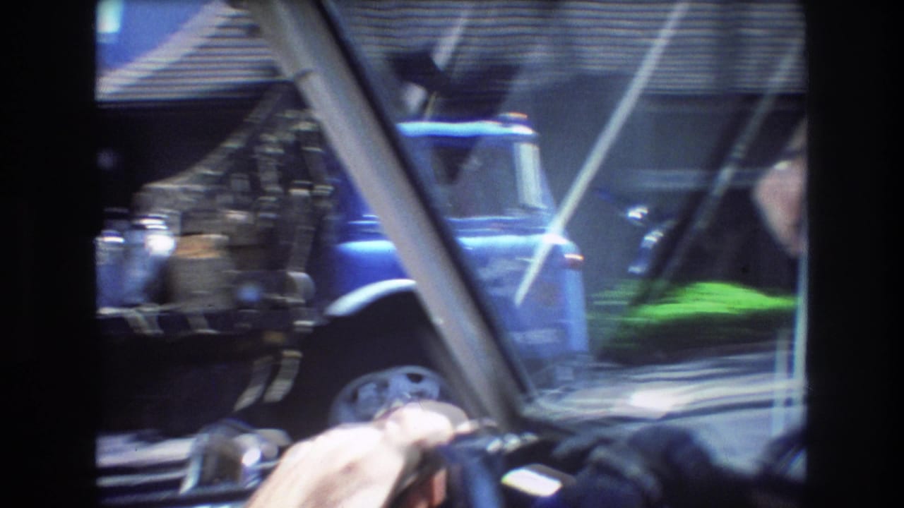 Windshield view from inside a moving car with a hand on the wheel and a blue truck outside.