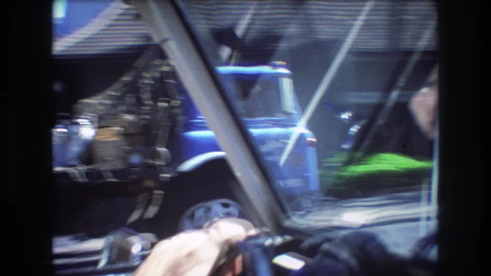 1977 Honolulu in-car driving view with windshield reflections, a driver hand on the steering wheel, and a blue truck moving past outside.