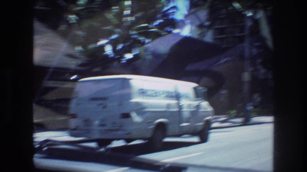 A white delivery van moves through a sunlit Honolulu street scene from 1977, with palm trees, roadside greenery, and high-rise buildings in soft 8mm focus.
