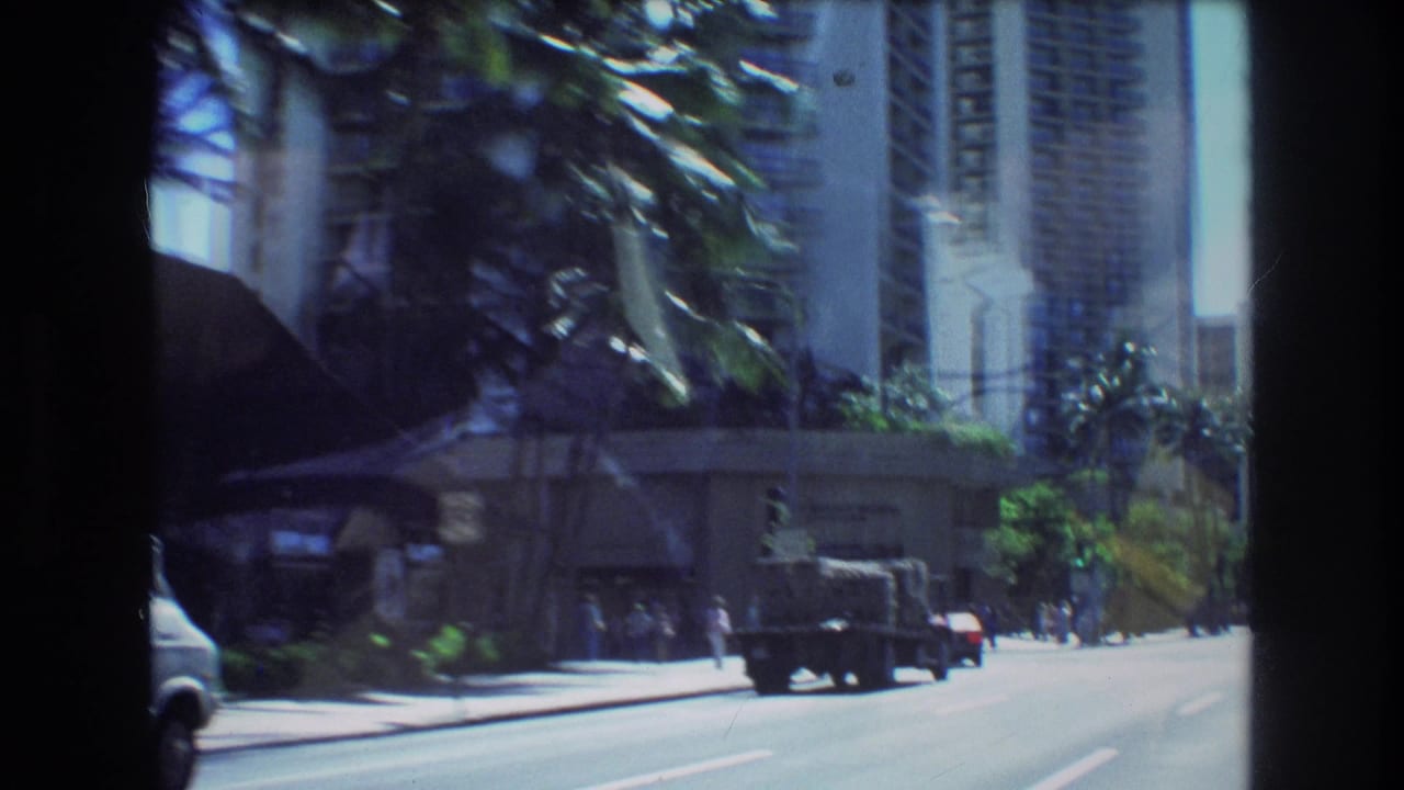 Dark truck drives along a broad city road bordered by palm trees and high-rises.