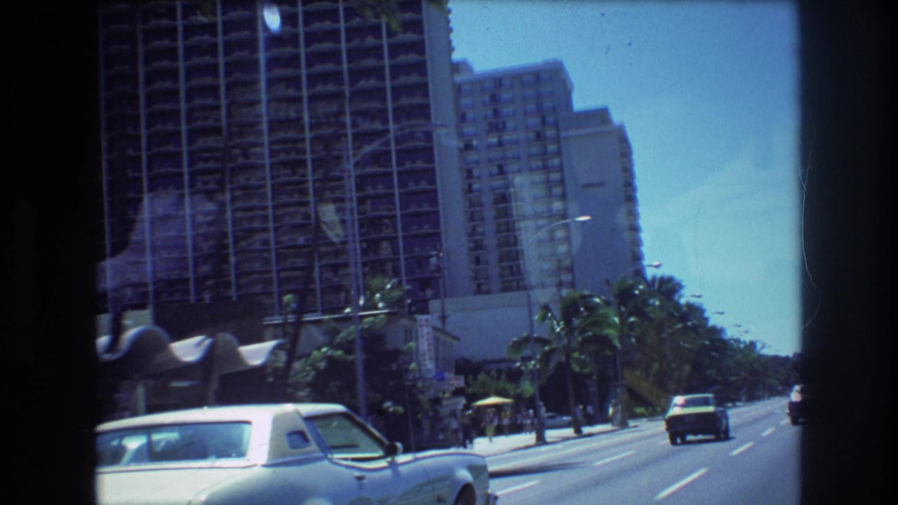 Palm-lined city street with high-rise hotels and a white coupe in the foreground.