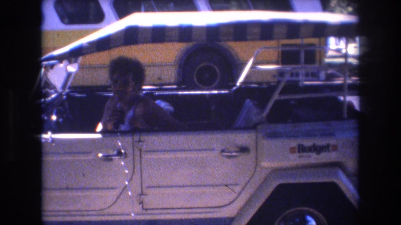 Person smiling from the driver's seat of a white open-top vehicle with a Budget bus behind.