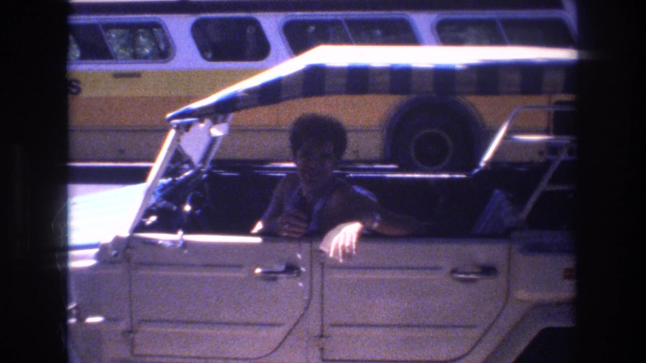 Man leaning in a white open-top car beside a yellow-and-white bus.