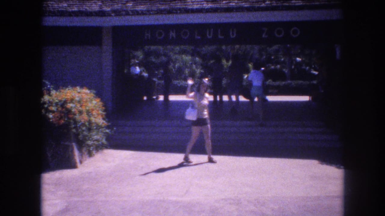 Woman standing and waving in front of the Honolulu Zoo entrance.