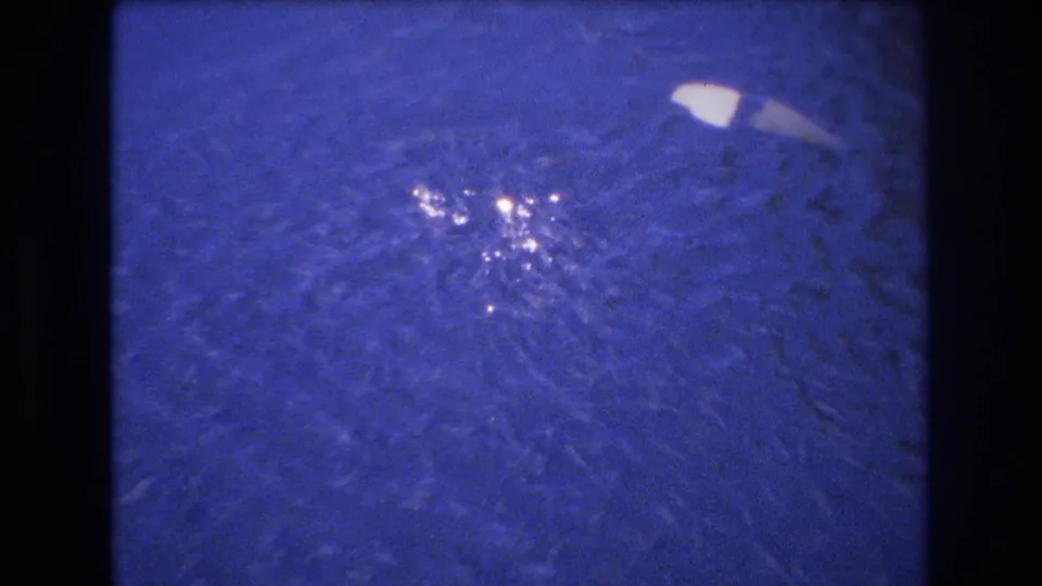 1977 Honolulu 8mm frame showing blue-tinted water, a bright floating piece, and a small splash or ripple pattern spreading outward.