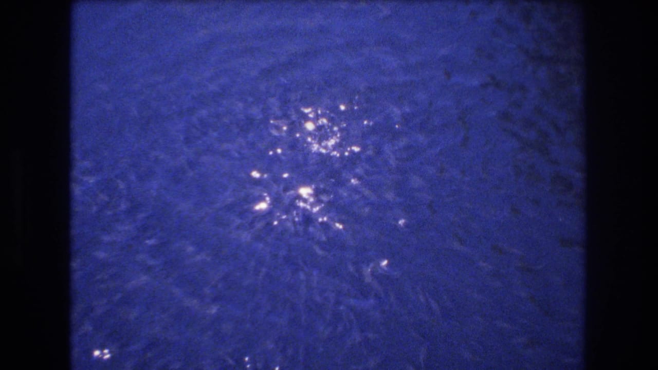 Blue-tinted rippling water in 1977 Honolulu home-movie footage, with bright sun reflections and dark 8mm frame edges.