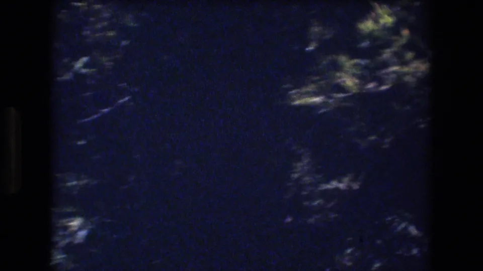Dark blurred tree foliage crosses patches of blue sky in a grainy 8mm Honolulu wind cutaway.