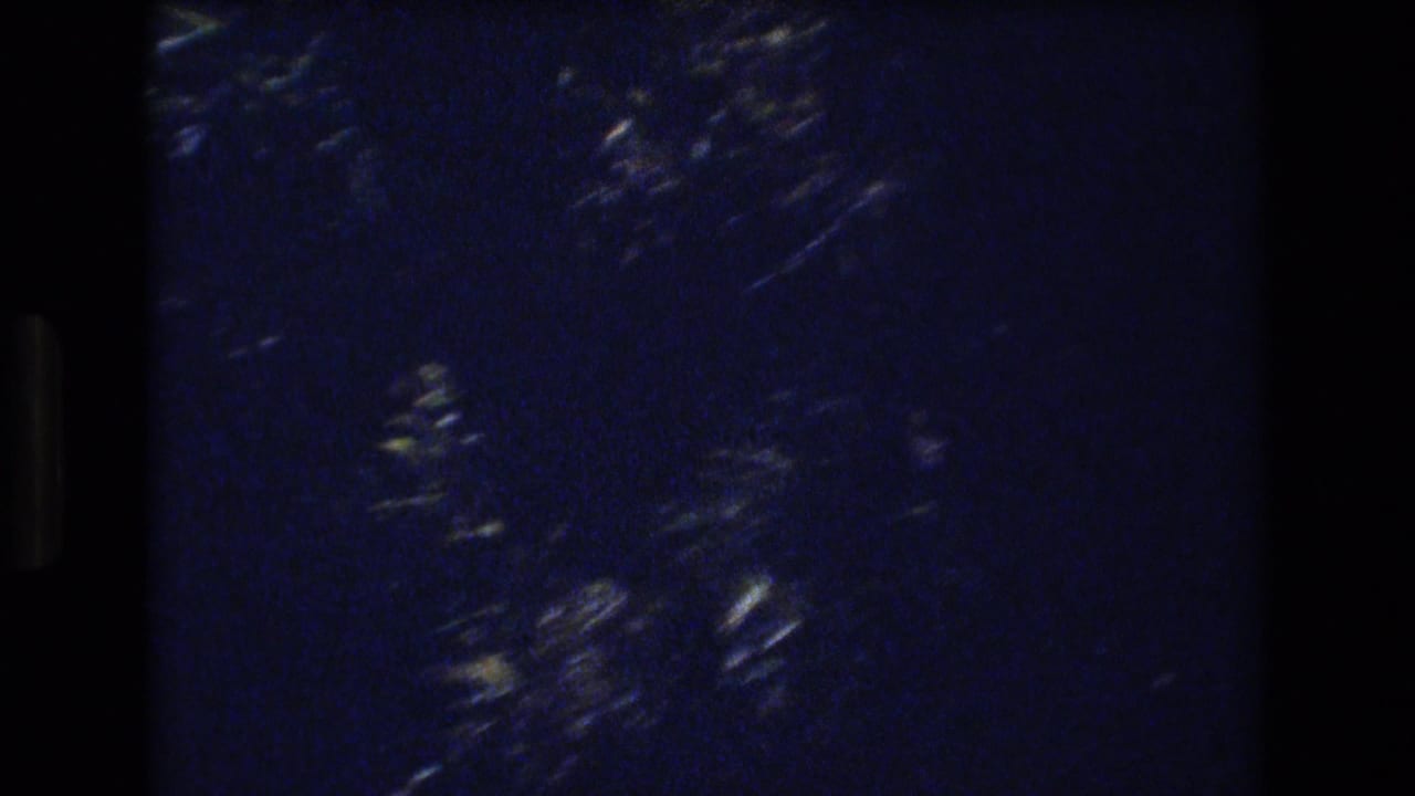 Dark blue-black 8mm frame with visible grain, soft light streaks, and no identifiable person or landmark.