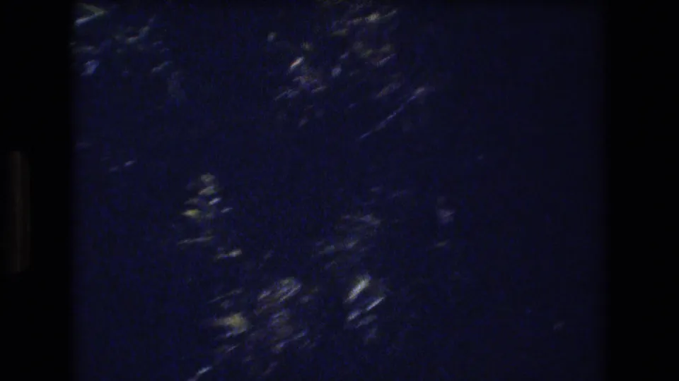 Dark blue-black 8mm frame with visible grain, soft light streaks, and no identifiable person or landmark.
