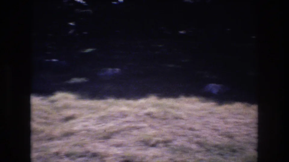 1977 Honolulu 8mm frame showing mostly shaded ground, indistinct rocks or debris, and a bright strip of grass along the bottom.