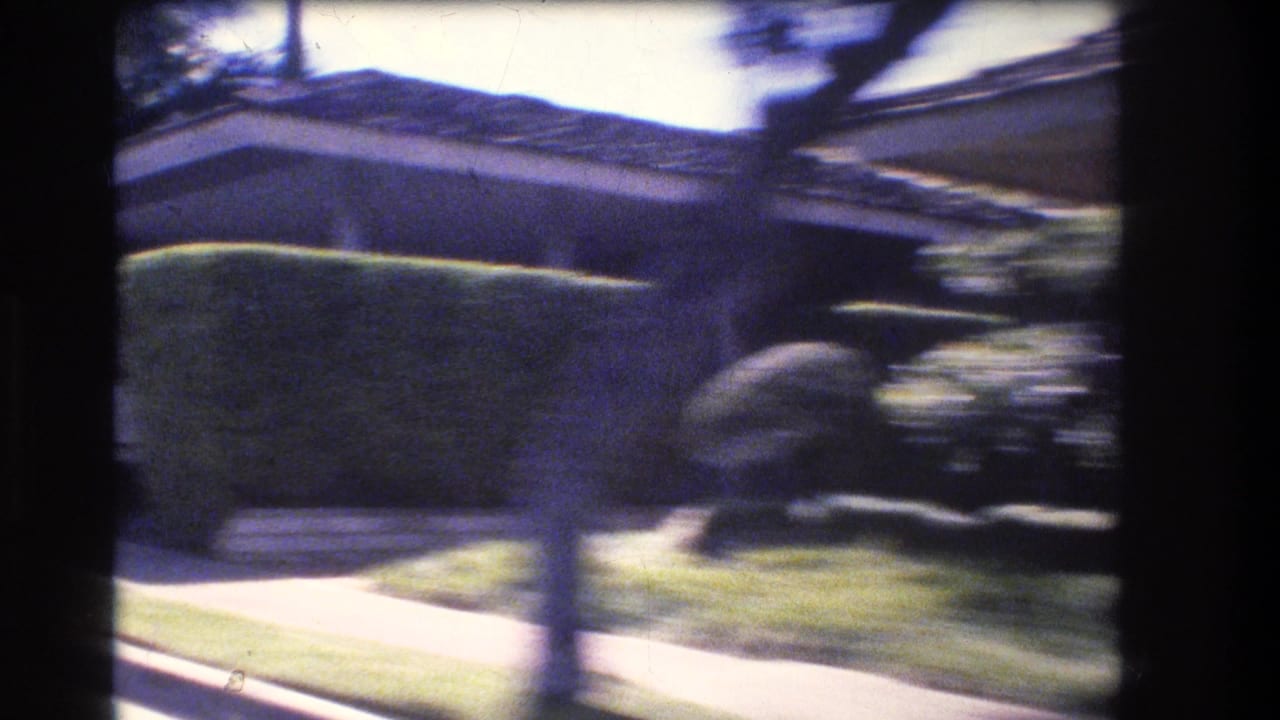 Low house behind a trimmed hedge with lawn, sidewalk, trees, and strong motion blur.