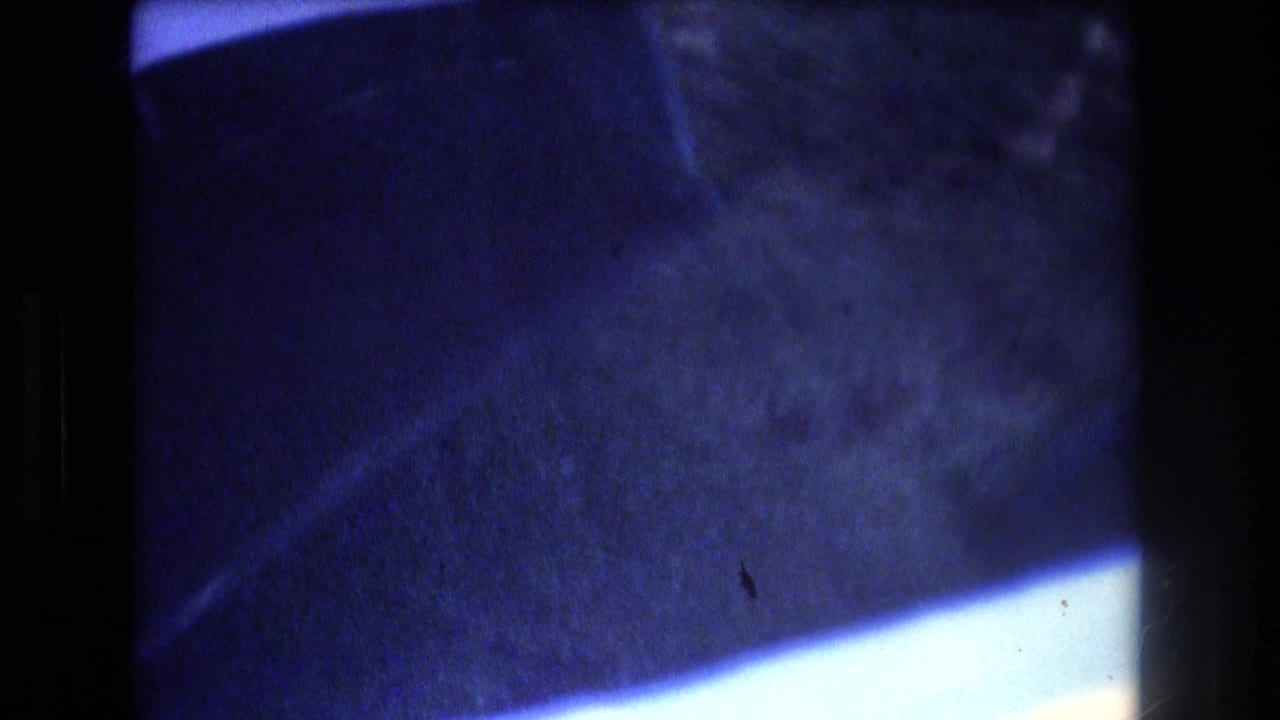 Blue water and dark boat or dock edges seen through a film frame.