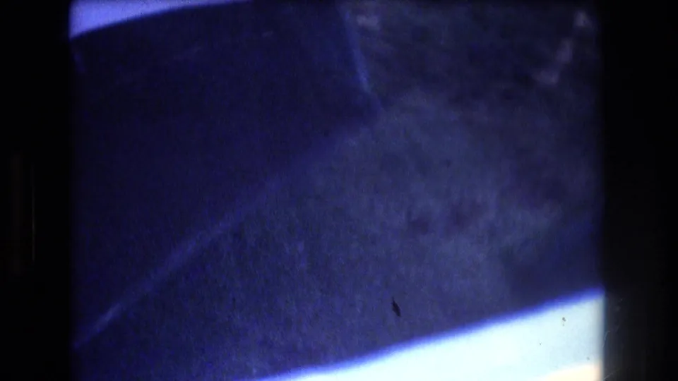 1977 Honolulu-area 8mm frame showing blue water beside dark boat or dock structure, with soft focus and visible film grain.