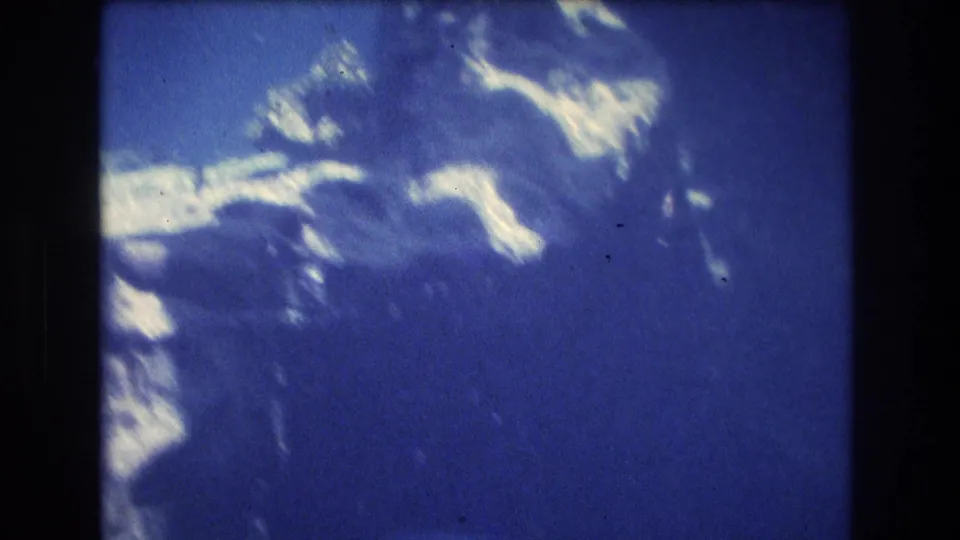 The final frame shows blue aquarium water with bright surface reflections and partial fish or rock shapes at the edge, retaining the soft 1970s 8mm look.