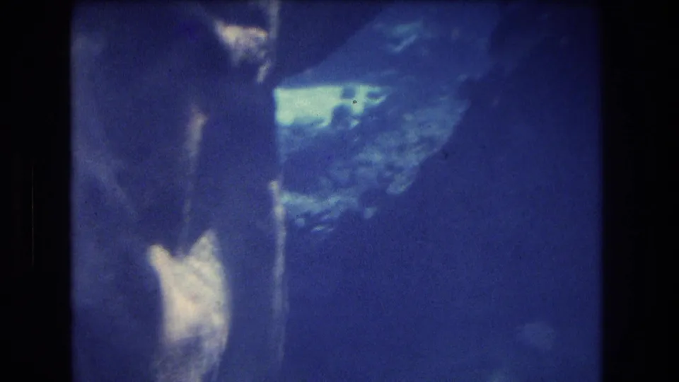 1977 Honolulu, Oahu underwater home-movie frame with blue water, bright reef patches, and soft indistinct coral or rock forms.