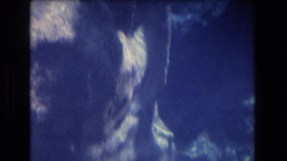 1977 Honolulu, Oahu 8mm underwater frame showing bright coral or rock shapes against dark blue water and blurred reef texture.