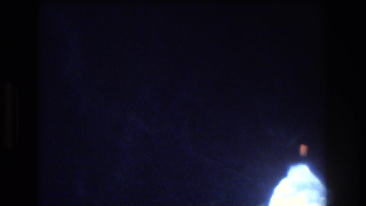 A mostly dark blue 8mm frame shows a small bright opening at the lower right, continuing the abstract underwater or cave-window view from the Honolulu-area clip.