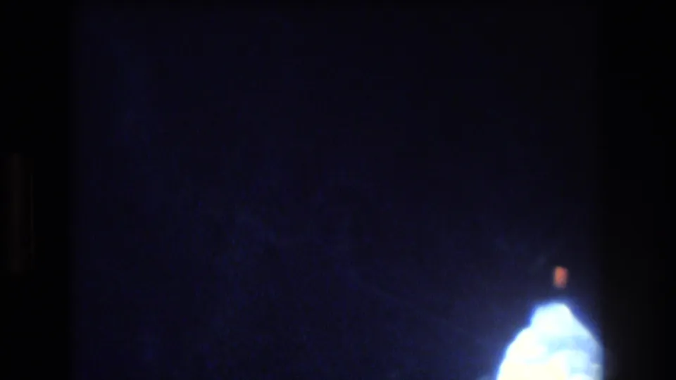 A mostly dark blue 8mm frame shows a small bright opening at the lower right, continuing the abstract underwater or cave-window view from the Honolulu-area clip.