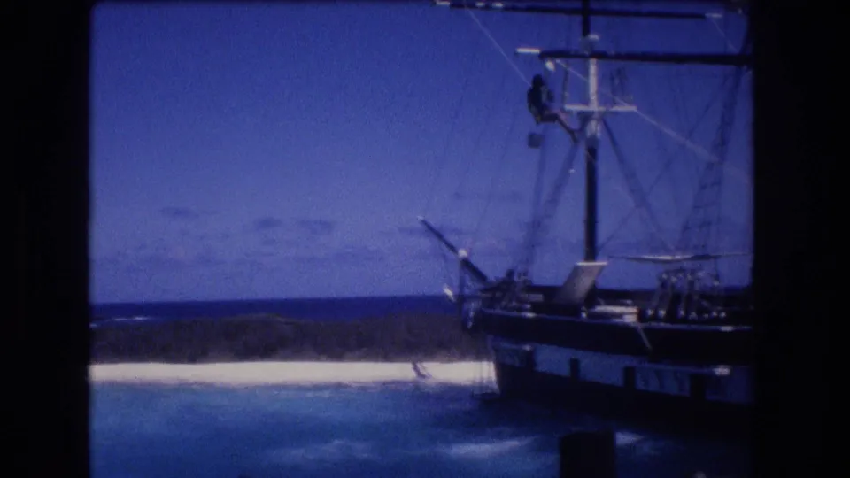 1977 Honolulu, Oahu 8mm frame showing a large sailing vessel wedged near a white sandbank, with rigging, blue water, and a crewman high on the mast.