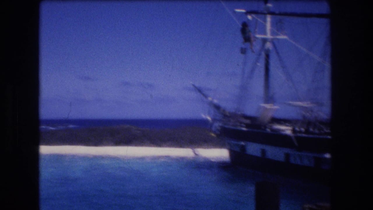 Sailing vessel at the right edge of the frame near turquoise water and a white sandbar.