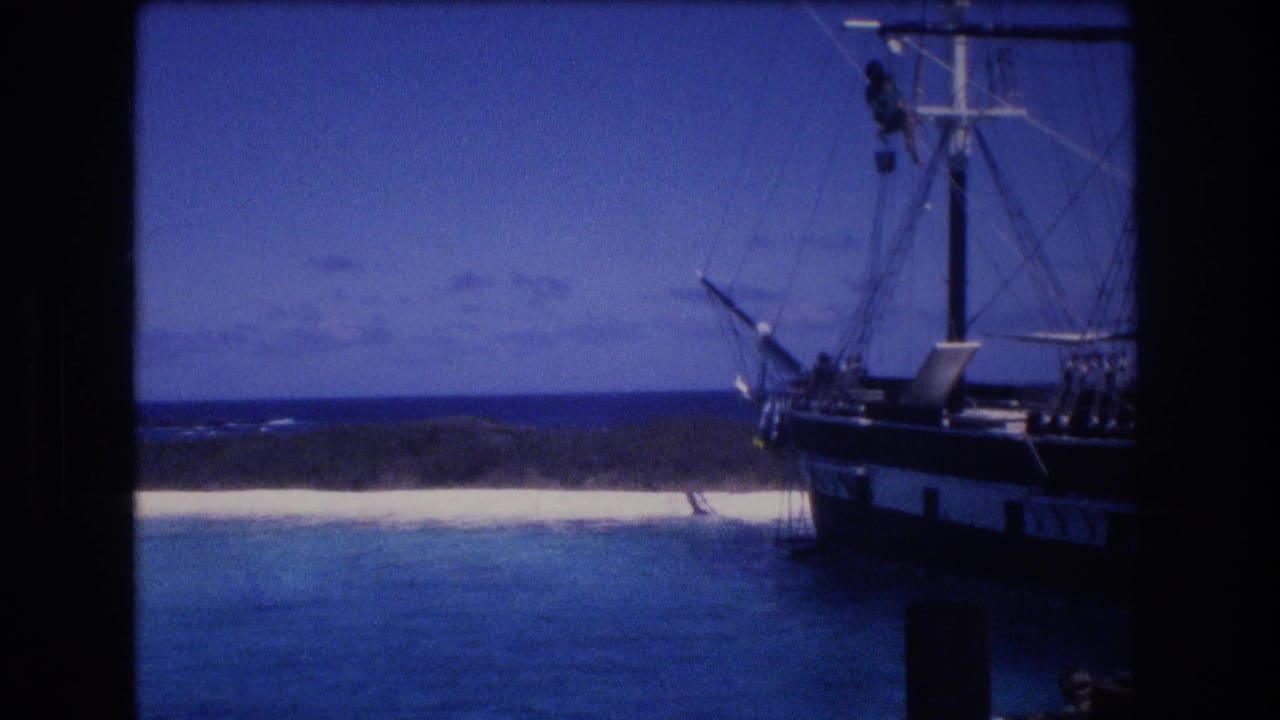 Sailing ship at the right edge of the frame with beach, water, and horizon behind it.
