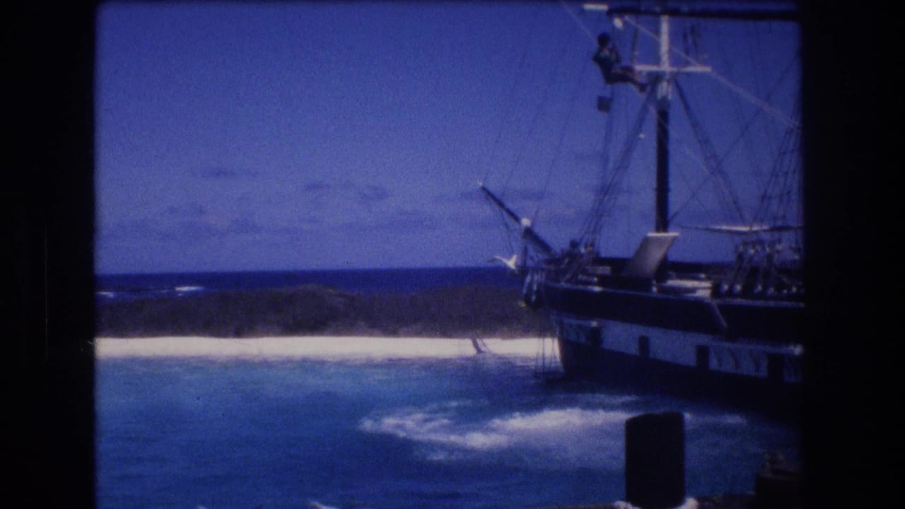 Moored sailing ship beside turquoise water and a white beach.