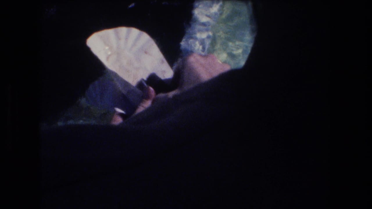 Hand near dark shoreline holding a pale folded item over blue-green water.