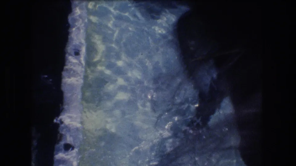1977 Honolulu home-movie frame focused on the clear water tank, with rippled blue water, tank structure, and a dark partial shape near the right edge.