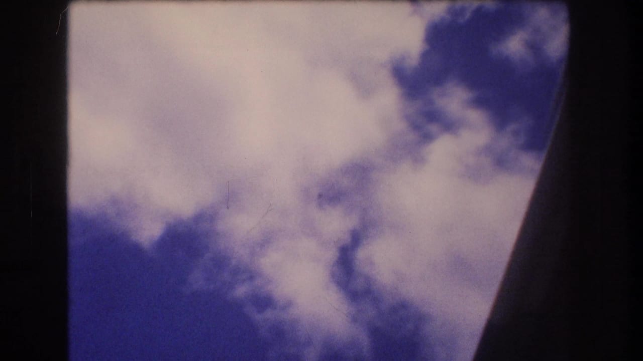 Abrupt 8mm sky frame from the Honolulu, Oahu clip showing pale clouds against blue sky with a dark curved film border at the right edge.