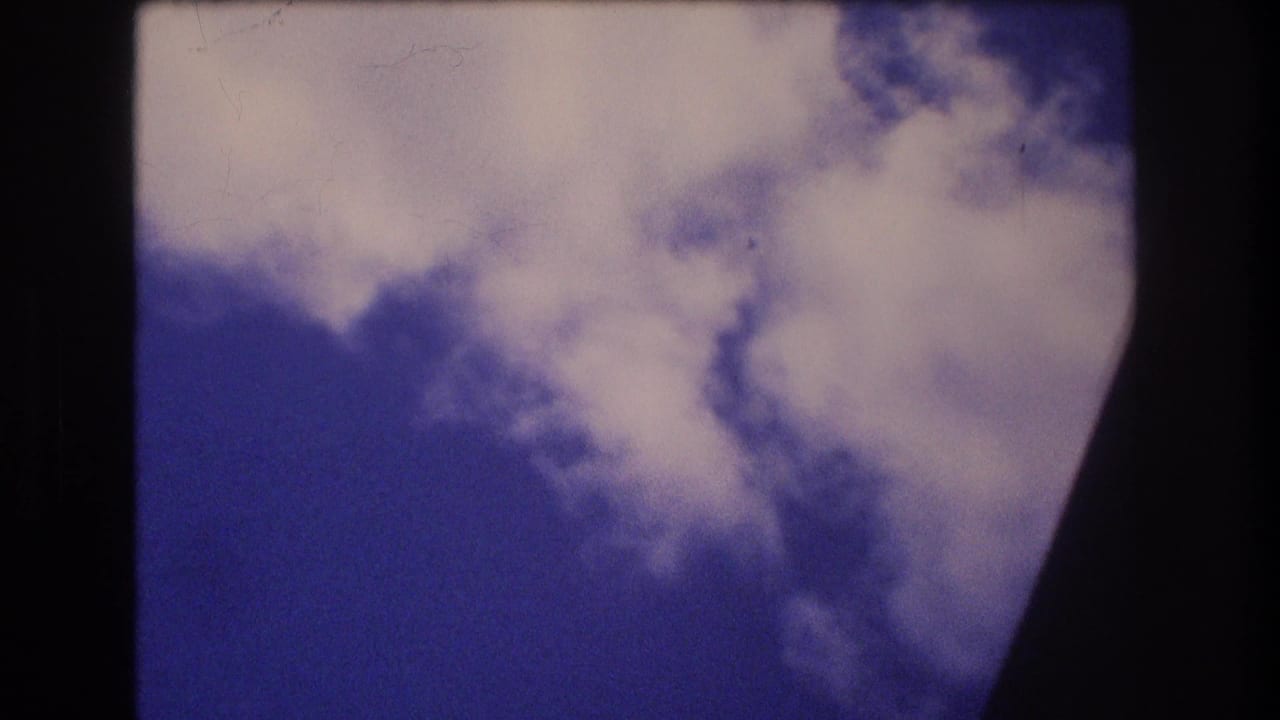Soft 8mm frame of clouds over blue sky seen from an airplane passenger window during a 1977 Honolulu Oahu trip.