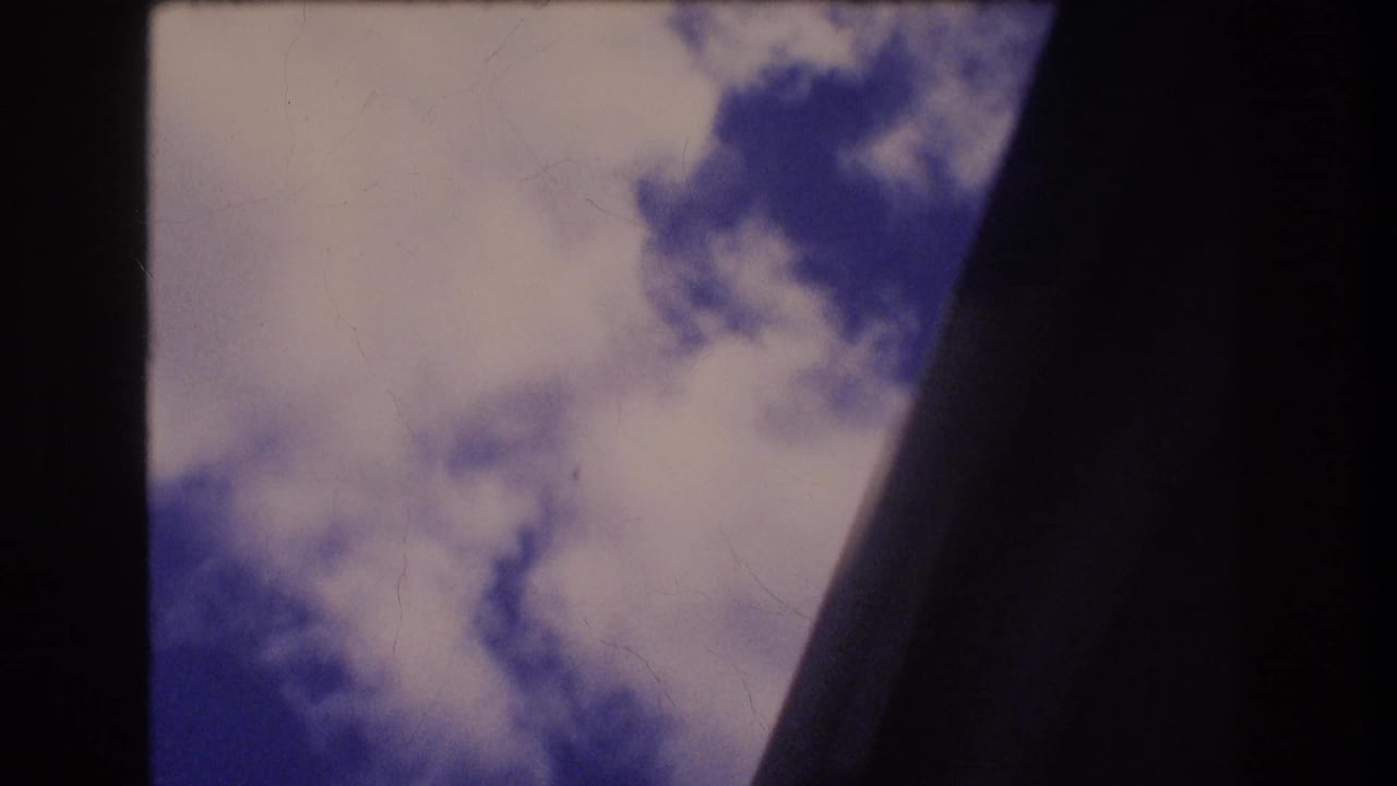 Final frame of metadata-supported 1977 Honolulu Oahu 8mm footage showing bright clouds through dark curved aircraft-window framing.