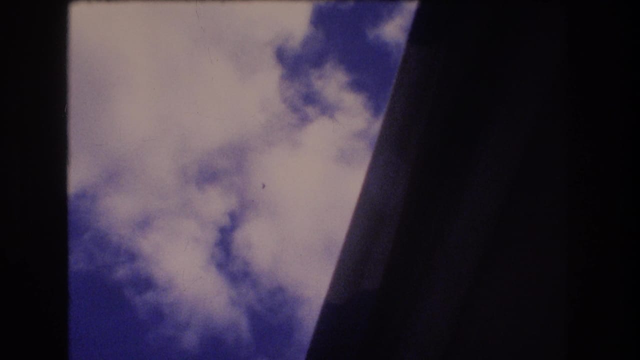 1977 Honolulu 8mm frame looking upward at blue sky and white clouds through dark structural or tree-like edges.