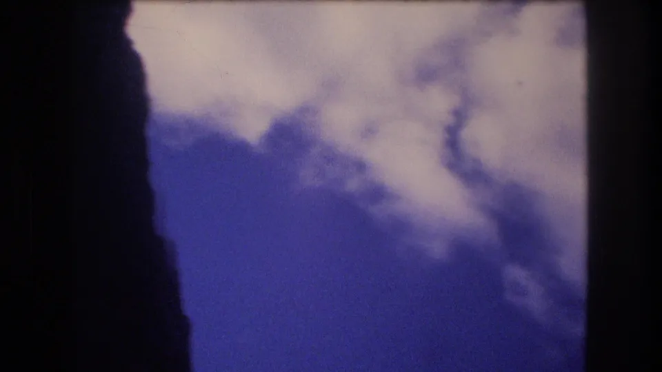 1977 Honolulu 8mm frame looking up at a bright cloud bank and blue sky between dark side framing shapes.