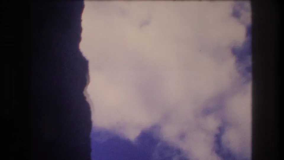 1977 Honolulu home-movie frame of a large white cloud filling much of the sky, bordered by dark vertical forms.