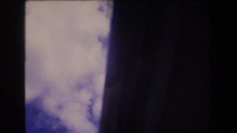 1977 Honolulu 8mm frame with bright white clouds against blue sky, partially blocked by dark vertical framing or window edges.