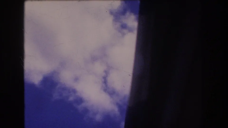 1977 Honolulu home-movie still showing a narrow upward view of blue sky and cloud beside a dark central edge, with aged 8mm film texture.