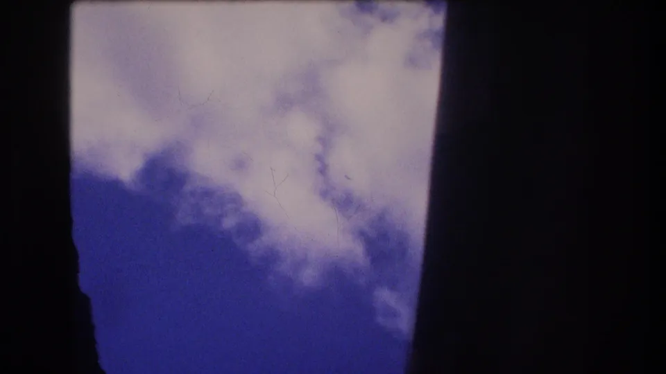 Cloudy blue sky remains visible through dark framing, with the 8mm scan showing soft contrast, dust marks, and blue-magenta color shift.