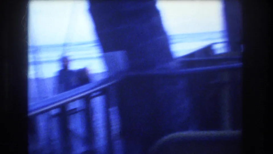 Soft 1977 8mm frame from the Honolulu boat scene with a blurred silhouetted figure, deck railing, and bright ocean horizon.