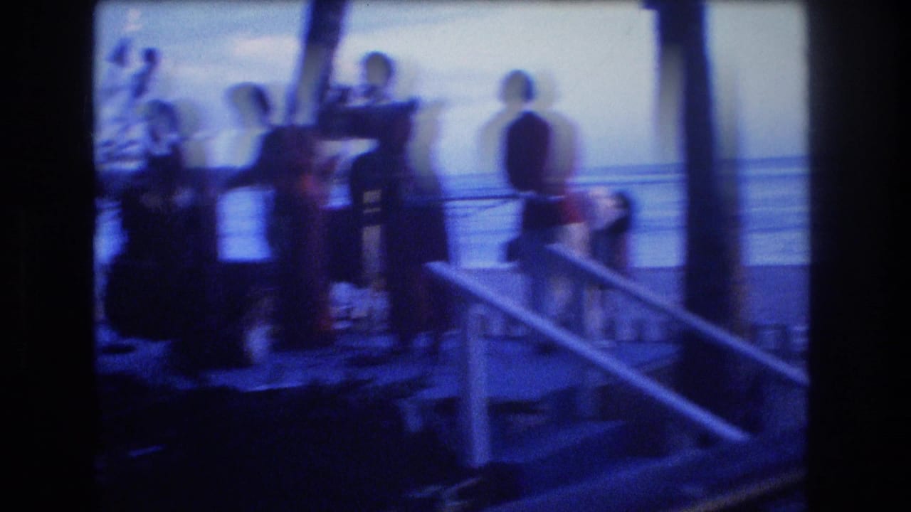 In 1977 Honolulu, Oahu home-movie footage, a small group of musicians appears on a platform near the ocean under a blue twilight sky.