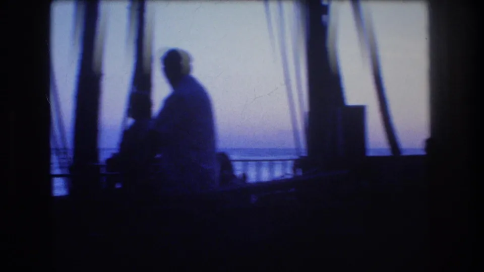 1977 Honolulu or Oahu 8mm frame showing silhouetted figures in a shaded lanai-like area overlooking the ocean through palm trunks.