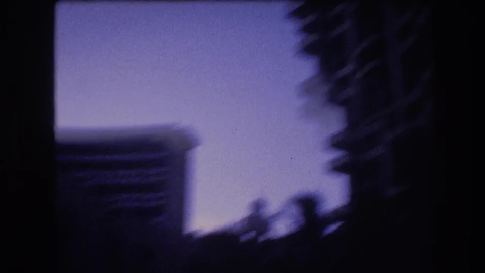 A soft 1977 Honolulu frame shows hotel towers and palm silhouettes in deep blue twilight, with the buildings only partly legible through motion blur.